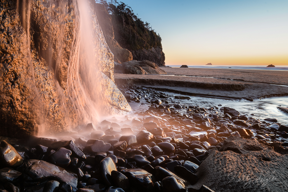The setting sun reflecting on a beautiful beach waterfall.